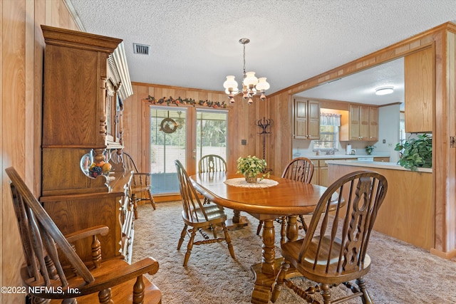 dining area with wood walls, a chandelier, light carpet, ornamental molding, and a textured ceiling