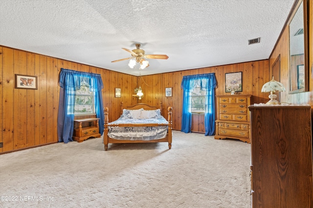 bedroom with ceiling fan, light colored carpet, a textured ceiling, and wood walls