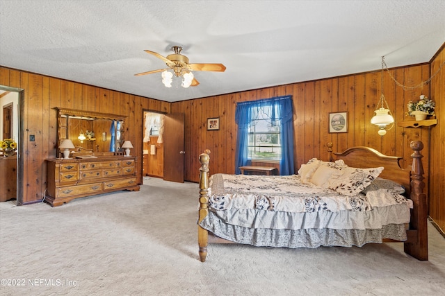 carpeted bedroom with ceiling fan, wood walls, and a textured ceiling