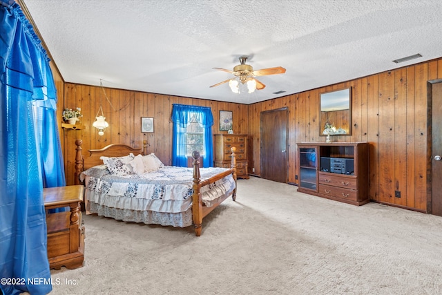 carpeted bedroom featuring wood walls, a textured ceiling, and ceiling fan