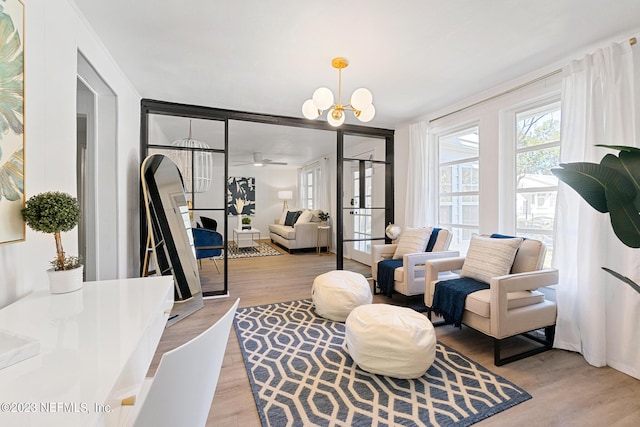 sitting room with ceiling fan with notable chandelier and light hardwood / wood-style flooring