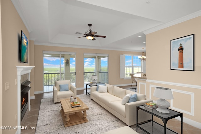 living room featuring tile patterned flooring, crown molding, ceiling fan with notable chandelier, and a tray ceiling