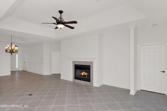 unfurnished living room with a fireplace, a raised ceiling, ceiling fan with notable chandelier, and light tile patterned floors