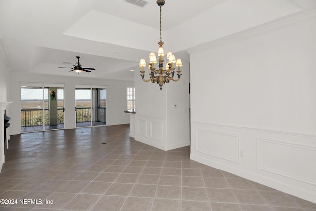 empty room with ceiling fan with notable chandelier, a healthy amount of sunlight, light tile patterned floors, and a tray ceiling