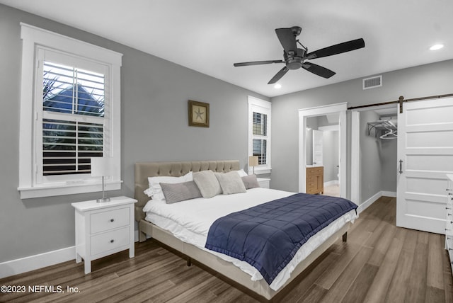 bedroom featuring hardwood / wood-style flooring, ensuite bath, a barn door, and a walk in closet