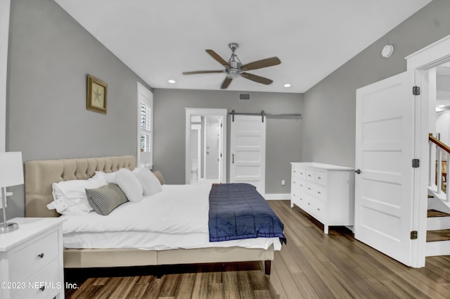 bedroom with wood-type flooring, a barn door, and ceiling fan