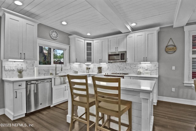 kitchen featuring appliances with stainless steel finishes, a center island, beamed ceiling, and dark hardwood / wood-style flooring