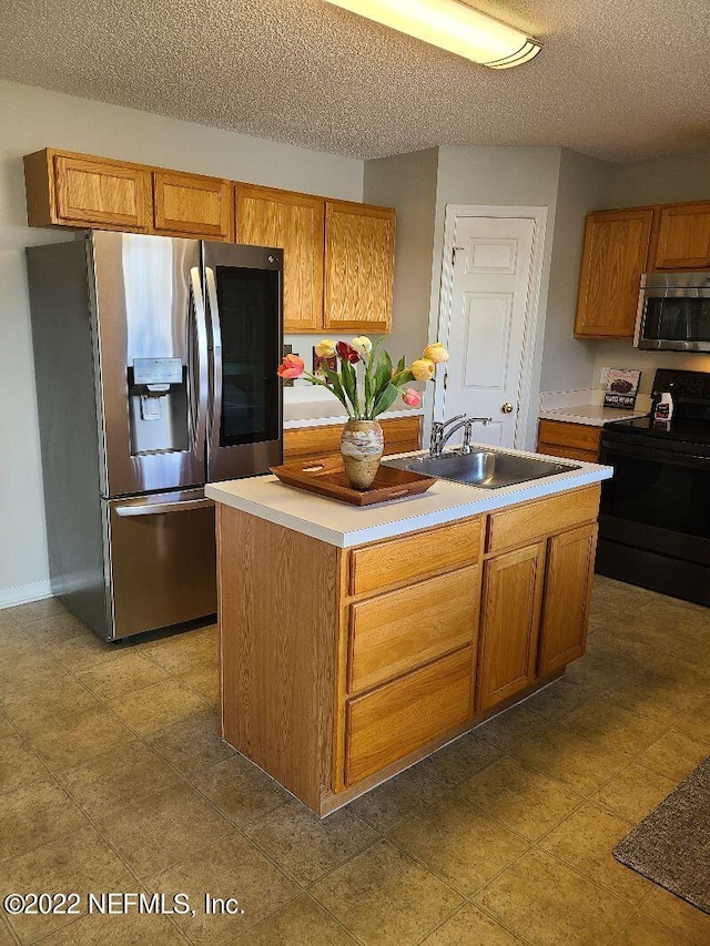 kitchen with a textured ceiling, stainless steel appliances, a center island with sink, and sink