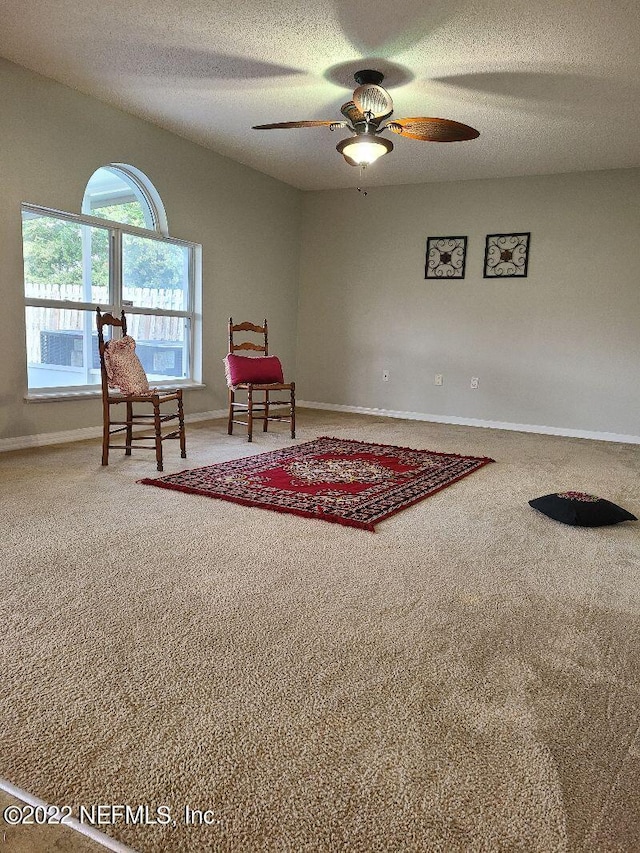 living area featuring ceiling fan, carpet floors, and a textured ceiling