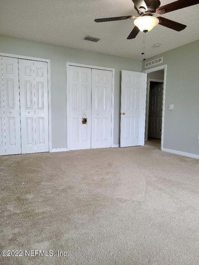 unfurnished bedroom with two closets, ceiling fan, carpet, and a textured ceiling