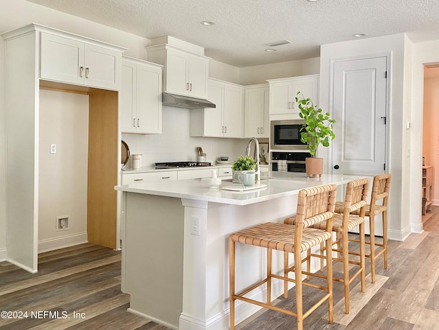 kitchen with a breakfast bar area, an island with sink, white cabinets, and appliances with stainless steel finishes