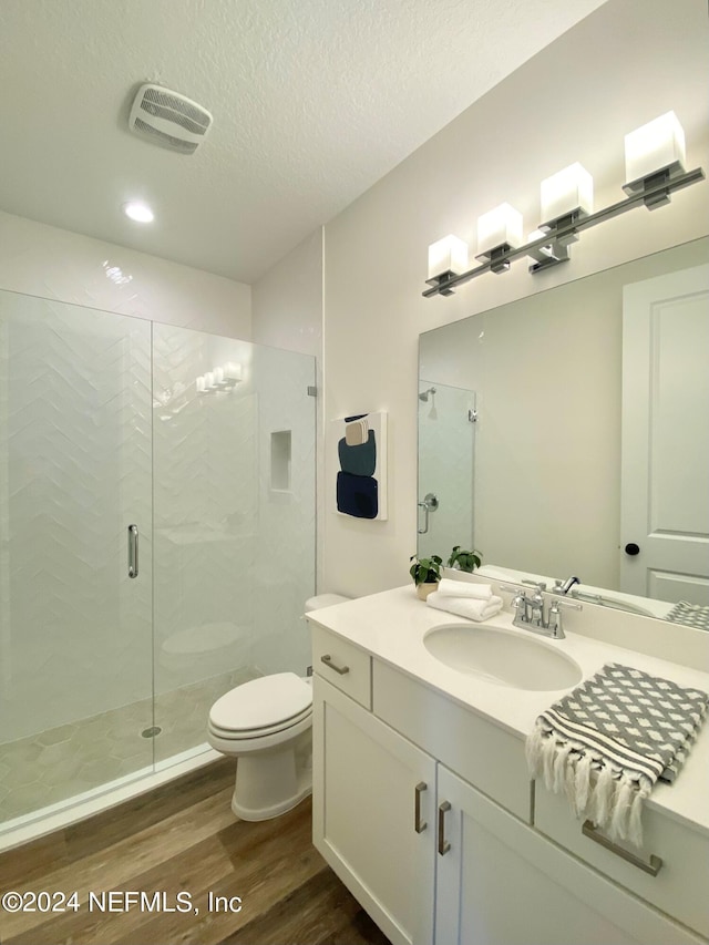 bathroom with a shower with door, hardwood / wood-style floors, vanity, a textured ceiling, and toilet