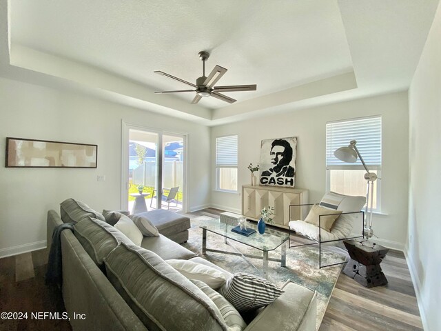 living room featuring ceiling fan, a tray ceiling, and light hardwood / wood-style floors