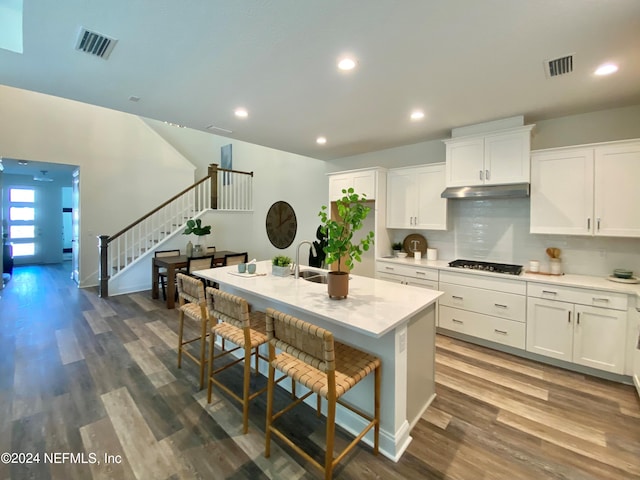 kitchen featuring a kitchen bar, white cabinetry, dark hardwood / wood-style floors, an island with sink, and backsplash