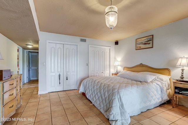 bedroom featuring a textured ceiling, light tile patterned floors, and multiple closets