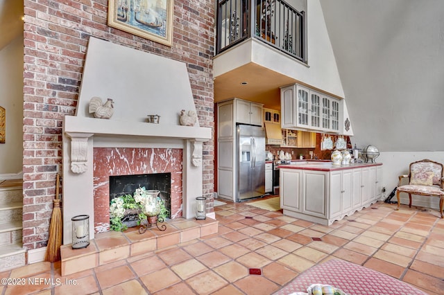 kitchen featuring a high ceiling, a tiled fireplace, light tile patterned floors, and stainless steel appliances