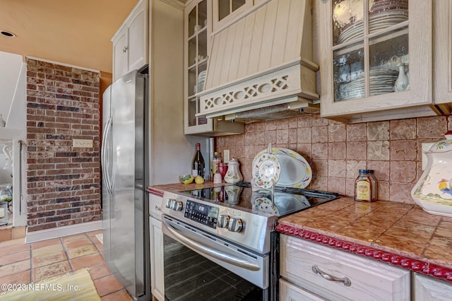 kitchen with decorative backsplash, cream cabinets, appliances with stainless steel finishes, and custom exhaust hood