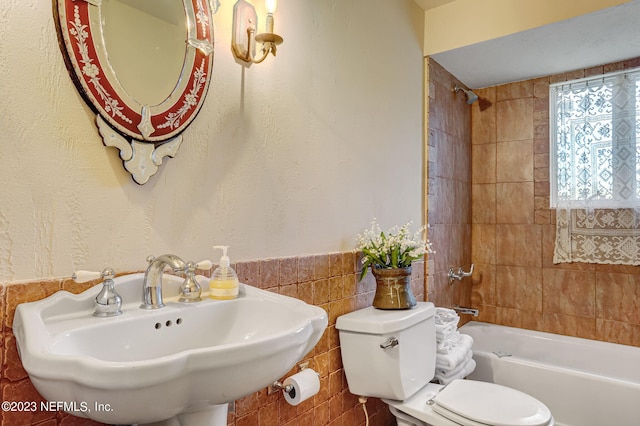 full bathroom featuring tile walls, sink, tiled shower / bath, and toilet