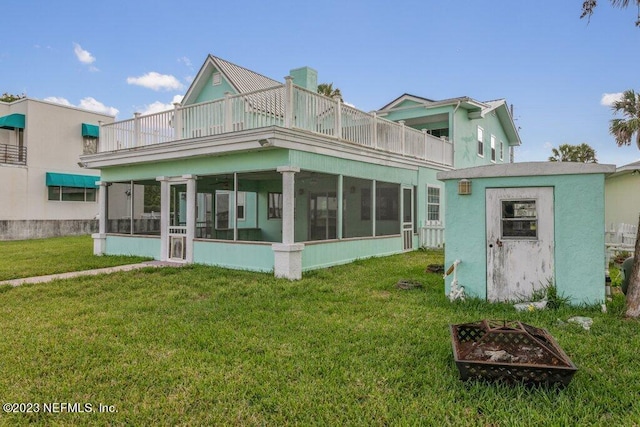 rear view of property with a balcony, a sunroom, a yard, and an outdoor fire pit