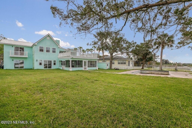 rear view of property with a balcony, a sunroom, and a yard