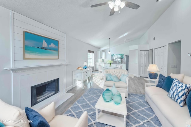 living room featuring a textured ceiling, vaulted ceiling, ceiling fan, light hardwood / wood-style flooring, and a fireplace