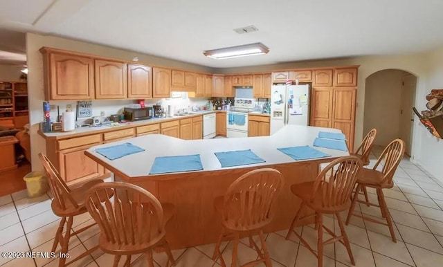 kitchen with white appliances, light brown cabinets, a center island, and light tile patterned floors