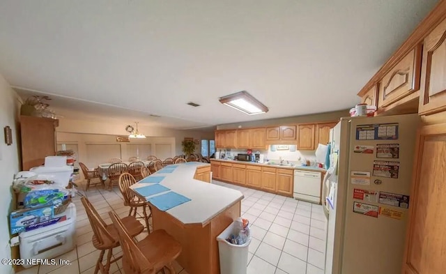 kitchen featuring sink, light tile patterned floors, white appliances, a center island, and light brown cabinetry