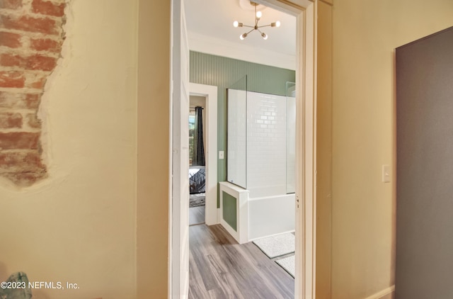 hallway with a notable chandelier, wood-type flooring, and crown molding