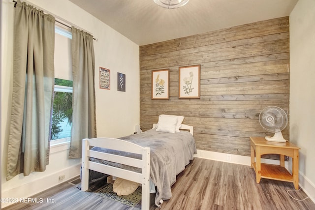 bedroom with multiple windows, wooden walls, and wood-type flooring