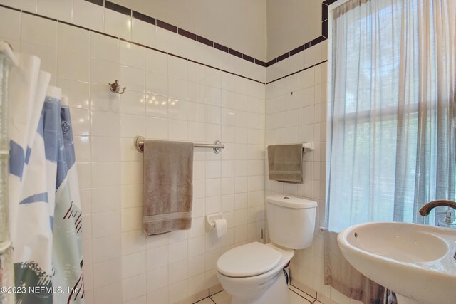 bathroom featuring tile walls, tile patterned floors, toilet, and sink