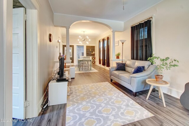 living room featuring hardwood / wood-style flooring, ornate columns, and an inviting chandelier