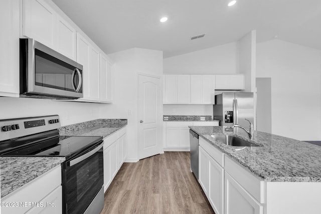 kitchen with sink, stainless steel appliances, vaulted ceiling, a kitchen island with sink, and white cabinets