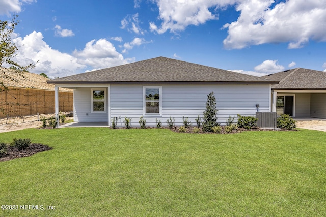 rear view of property with a yard, roof with shingles, fence, and central AC unit