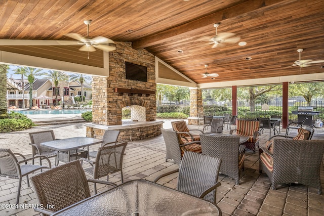 view of patio featuring an outdoor stone fireplace, grilling area, outdoor dining space, fence, and a community pool