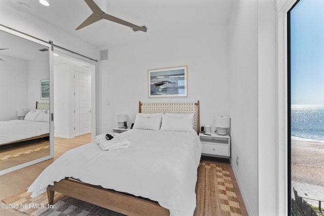 bedroom with a barn door, ceiling fan, and light hardwood / wood-style floors