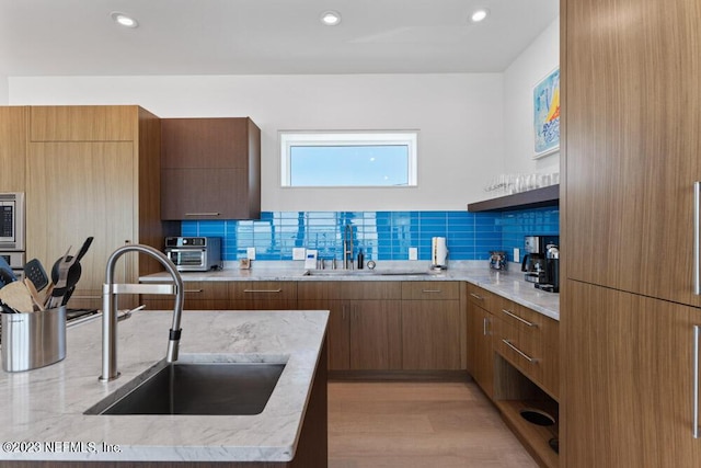 kitchen with tasteful backsplash, light stone countertops, sink, and light hardwood / wood-style flooring