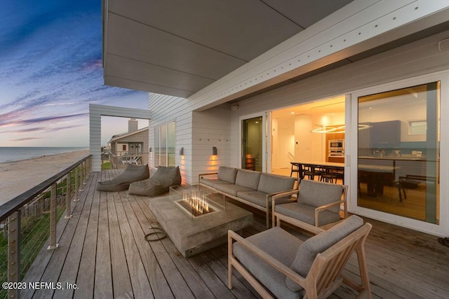 deck at dusk featuring a water view and an outdoor living space with a fire pit