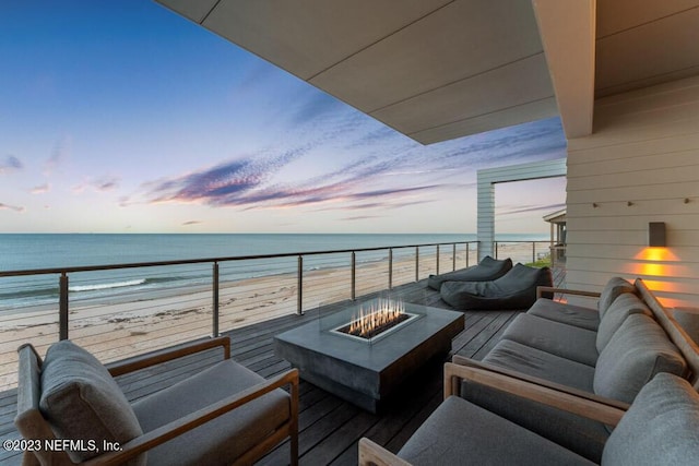 balcony at dusk with a beach view, a water view, and an outdoor living space with a fire pit