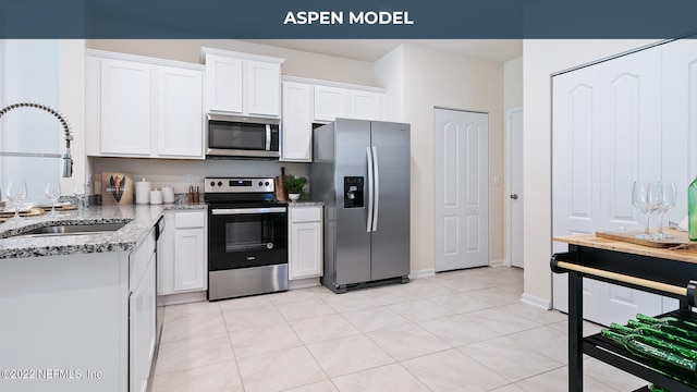 kitchen with white cabinets, light stone counters, appliances with stainless steel finishes, a sink, and light tile patterned flooring