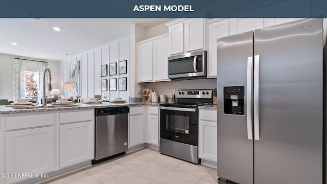 kitchen featuring light stone counters, appliances with stainless steel finishes, white cabinets, and a sink