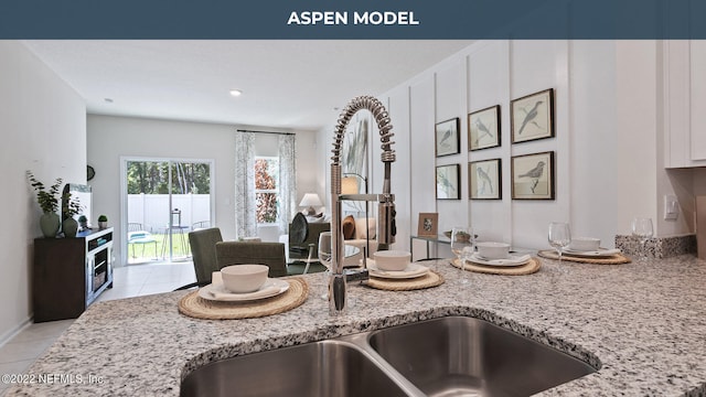 kitchen featuring light stone countertops, light tile patterned floors, white cabinets, and a sink