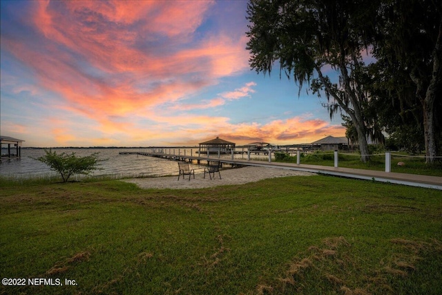 view of dock with a lawn and a water view