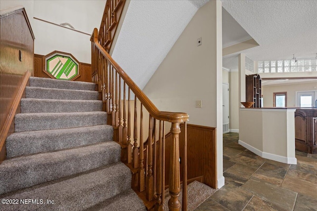 stairs with a textured ceiling, wood walls, and ornamental molding