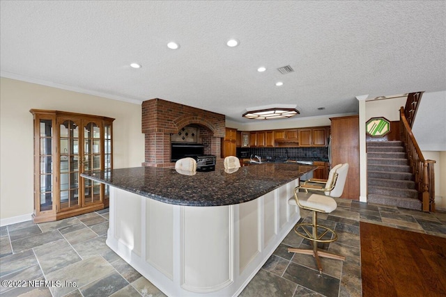 kitchen with dark stone counters, a textured ceiling, tasteful backsplash, a kitchen bar, and crown molding