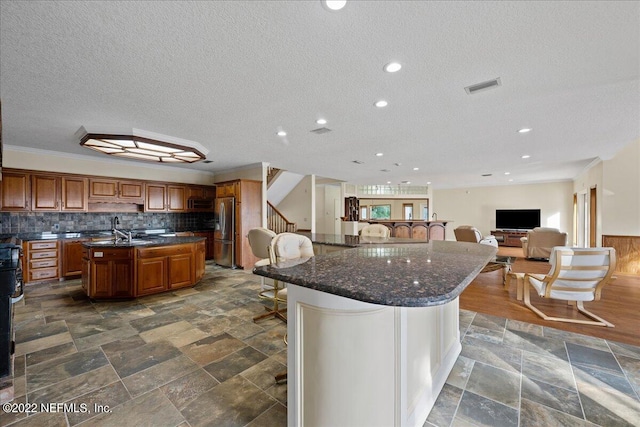 kitchen with stainless steel fridge, decorative backsplash, a textured ceiling, crown molding, and a kitchen island with sink