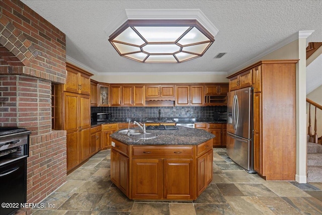 kitchen with decorative backsplash, dark stone countertops, stainless steel refrigerator with ice dispenser, a kitchen island with sink, and sink