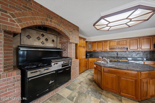 kitchen featuring dark stone countertops, an island with sink, backsplash, crown molding, and sink