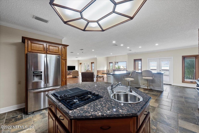 kitchen with a kitchen island with sink, sink, black gas stovetop, ornamental molding, and stainless steel fridge