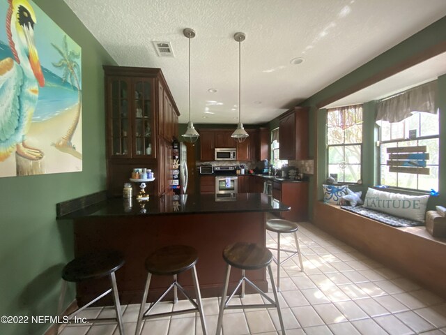 kitchen featuring a textured ceiling, decorative light fixtures, kitchen peninsula, a breakfast bar, and appliances with stainless steel finishes