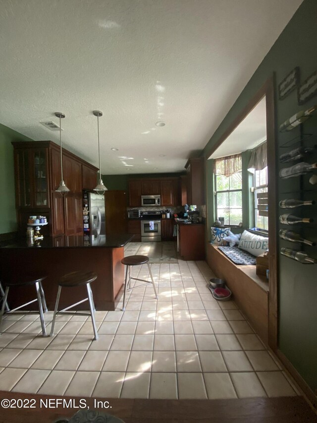 kitchen with pendant lighting, a textured ceiling, light tile patterned floors, a breakfast bar, and appliances with stainless steel finishes